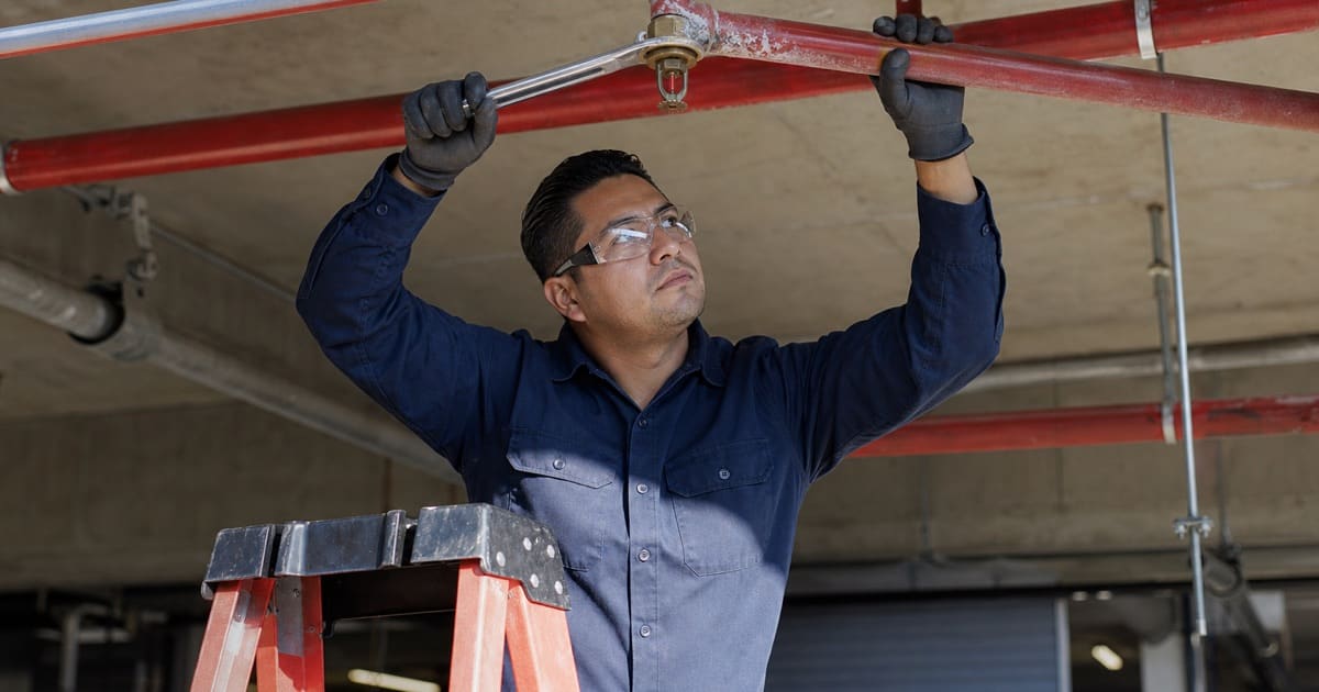 Technician replacing a sprinkler head on overhead branch line piping