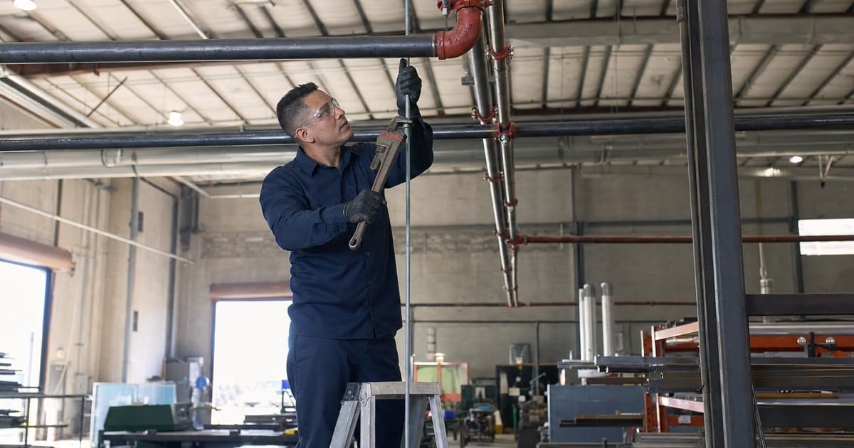Technician servicing sprinkler piping in a manufacturing building