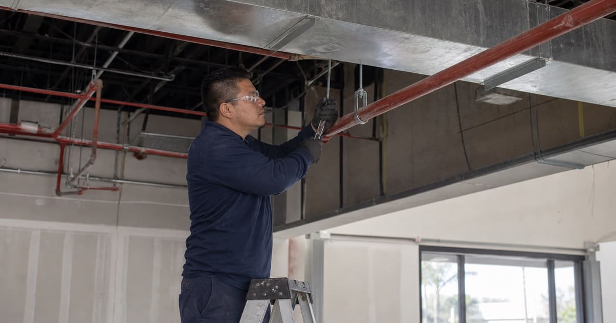 Technician adjusting a sprinkler pipe hanger in a renovated commercial building